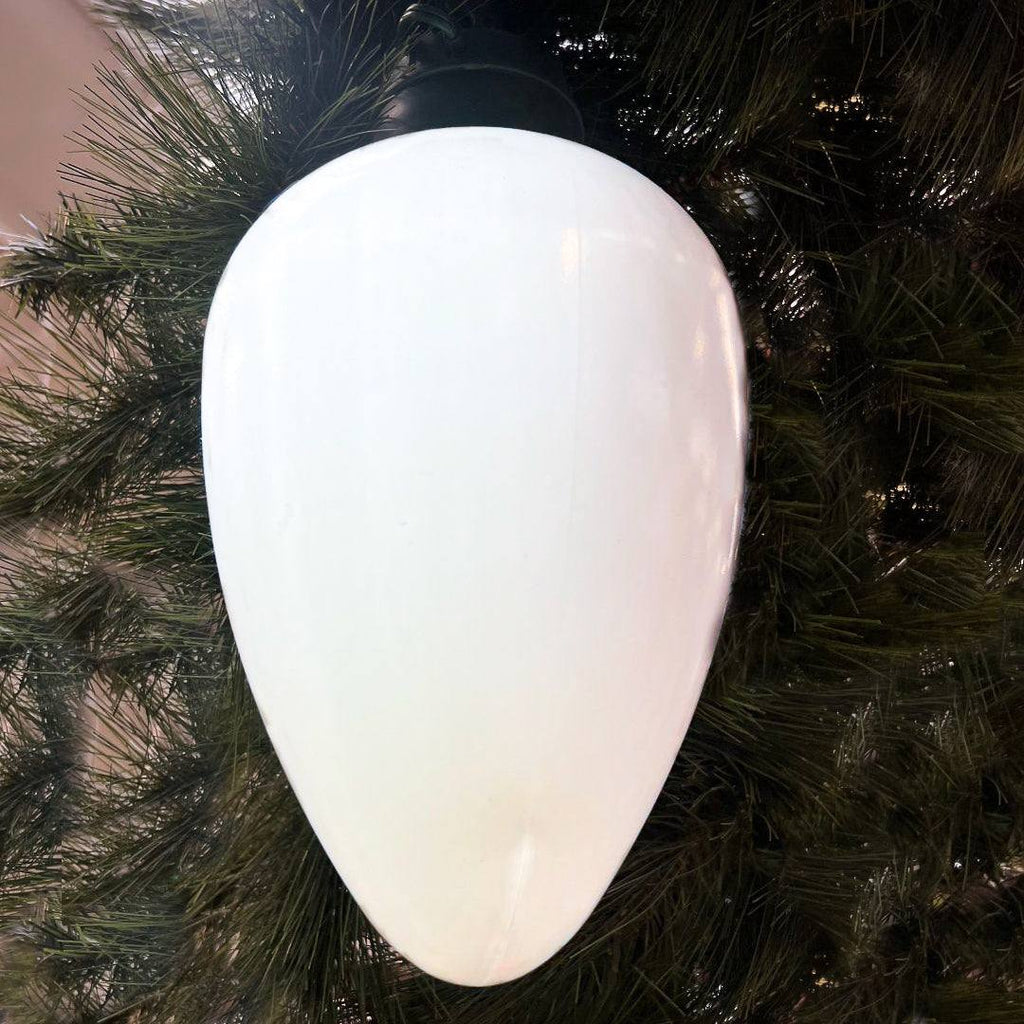 The Jumbo LED Lit Bulb - White by All Delivery Options hangs among green artificial pine branches, its smooth white surface reflecting colorful retro C9 lights.
