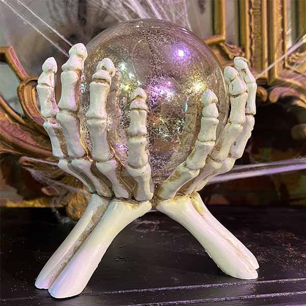 The Skeleton Hands Holding Crystal Ball by Available for Pick-Up & Delivery features skeletal hands with a crystal ball against ornate vintage mirrors and cobwebs. Its perfect for creating a spooky Halloween ambiance.