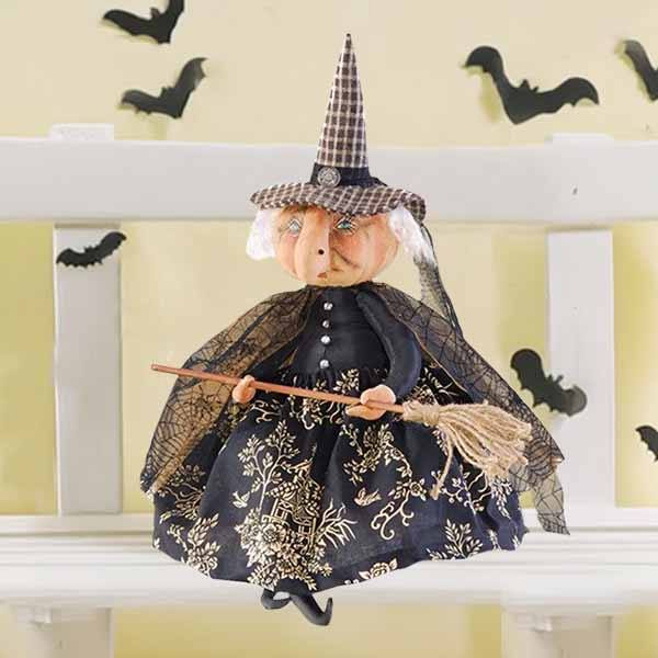The Witch - Naomi - 23 doll by Available for Pick-Up & Delivery showcases a hand-painted face, a plaid pointed hat, and a black dress with gold patterns. Shes seated on a white bench holding her broom beneath black bat wall decorations.