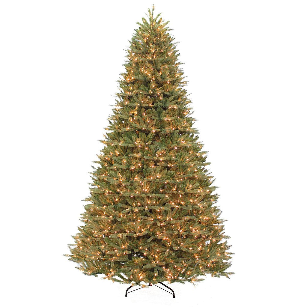 The Wyoming Fir Warm White LED Lights 10 Ft. is a tall artificial Christmas tree with dense green branches and numerous small glowing white lights, featuring a realistic design. It stands on a black metal stand against a plain white background, capturing the essence of a pre-lit tree.