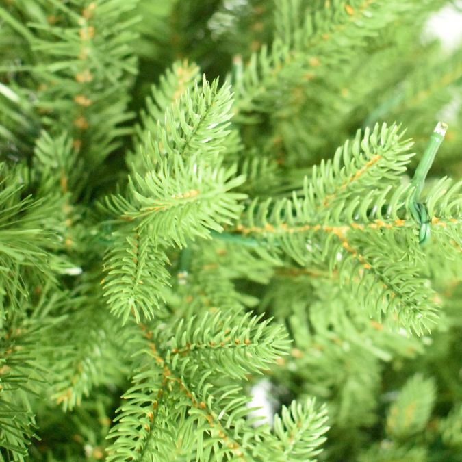 Close-up of green artificial balsam fir branches from a Balsam Fir Multi-Function Lights 5 Ft. Christmas tree, interwoven with small string lights.