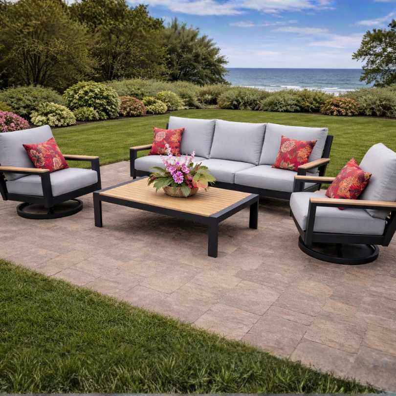 The Bozania 4-Piece Outdoor Patio Seating Set by Delivery Only features a gray-cushioned sofa, two armchairs with red floral pillows, and a teak coffee table, perfect for relaxing on your patio with lawn and ocean views.