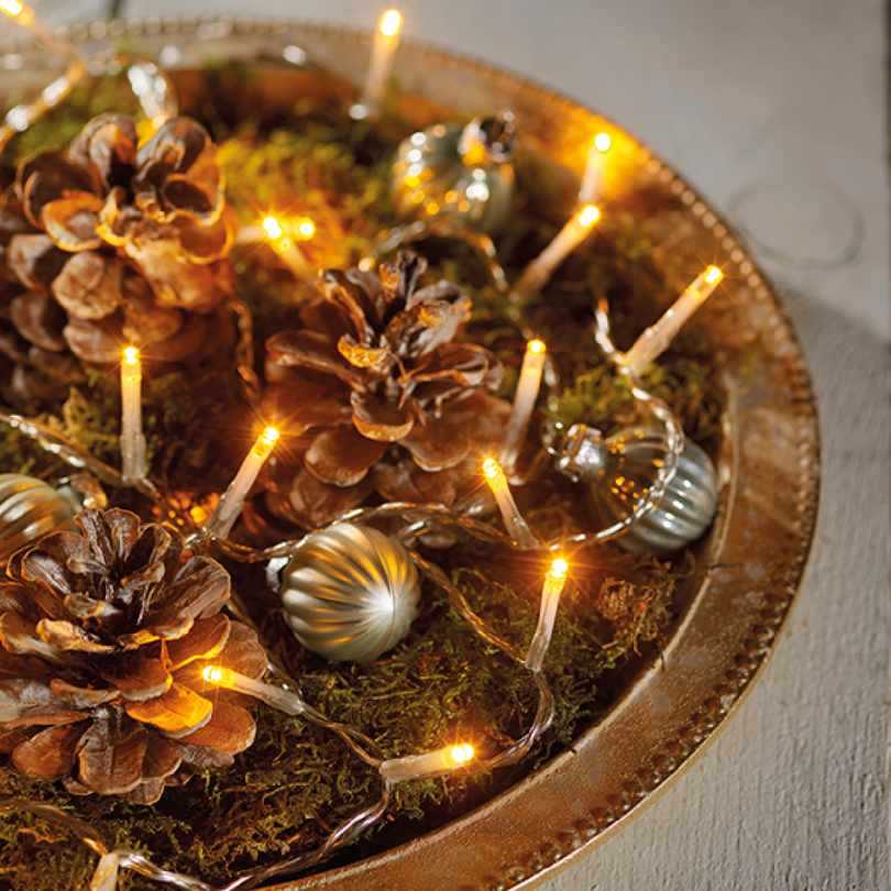 A festive holiday centerpiece features pinecones, green moss, silver ornaments, and Durawise Battery Operated LED Twinkle String Lights – Warm White from Available for Pick-Up & Delivery glowing warmly.