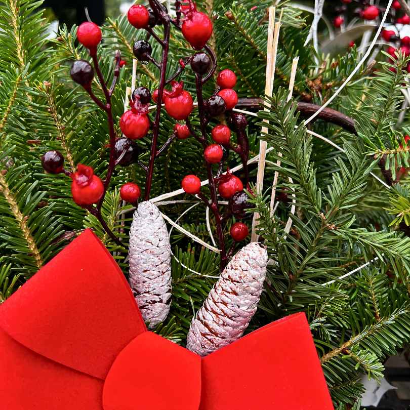 The Holiday Mini Log with Handle by Available for Pick-Up & Delivery features festive greens, red berries, white-tipped pinecones, curly silver twigs, and a red velvet bow for charming rustic holiday décor.