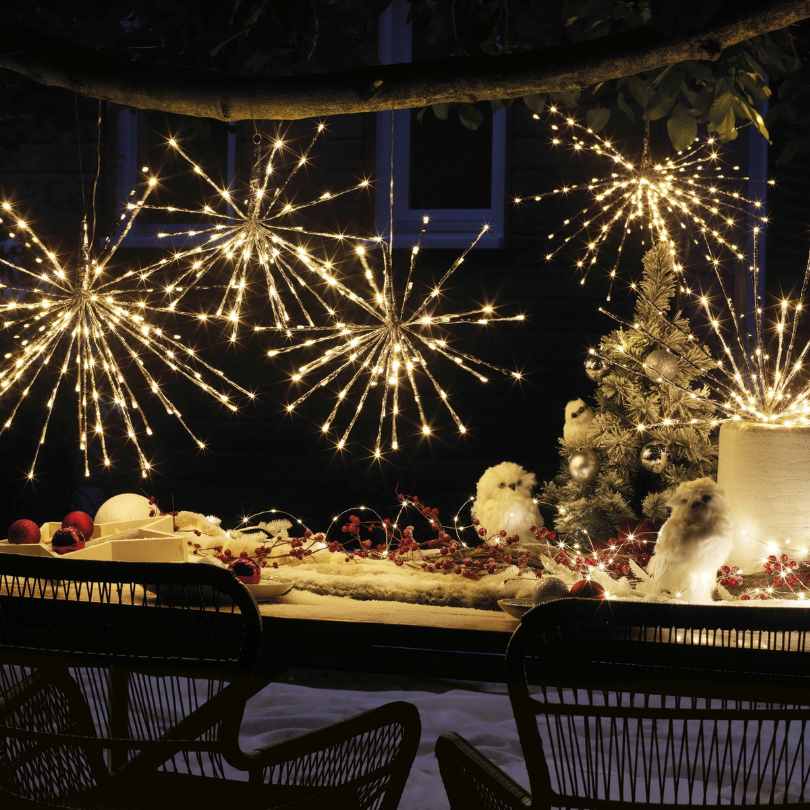 A festive outdoor table with Polestar Flashing LED 72 ct. Decoration Warm White by Available for Pick-Up & Delivery, a lit mini tree, artificial snow, white owls, and red ornaments creates cozy holiday décor with warm white LEDs at night.