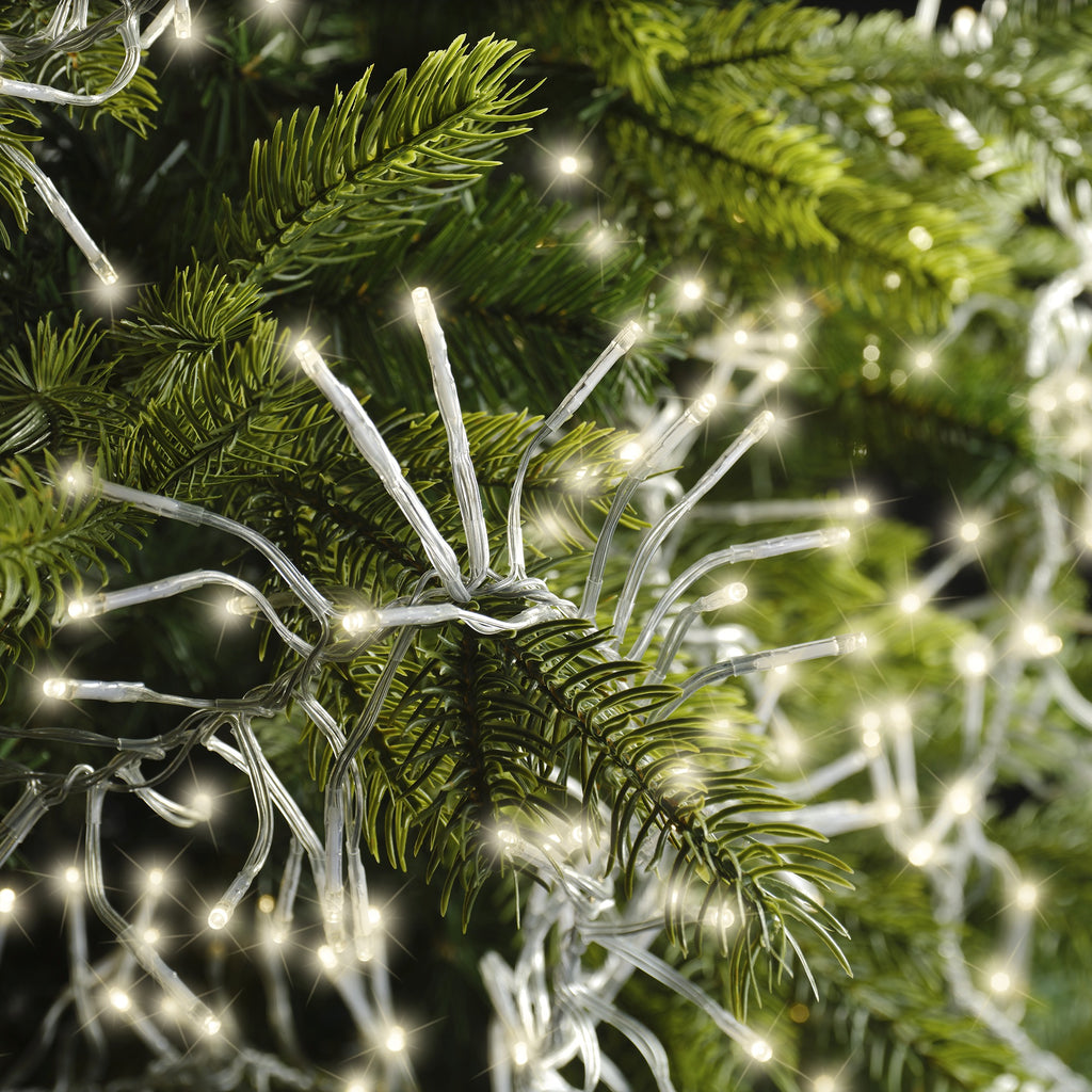 Close-up of green pine branches decorated with Cluster LED 768 ct. String Lights Warm White by Available for Pickup & Delivery, softly glowing and creating a festive holiday atmosphere.