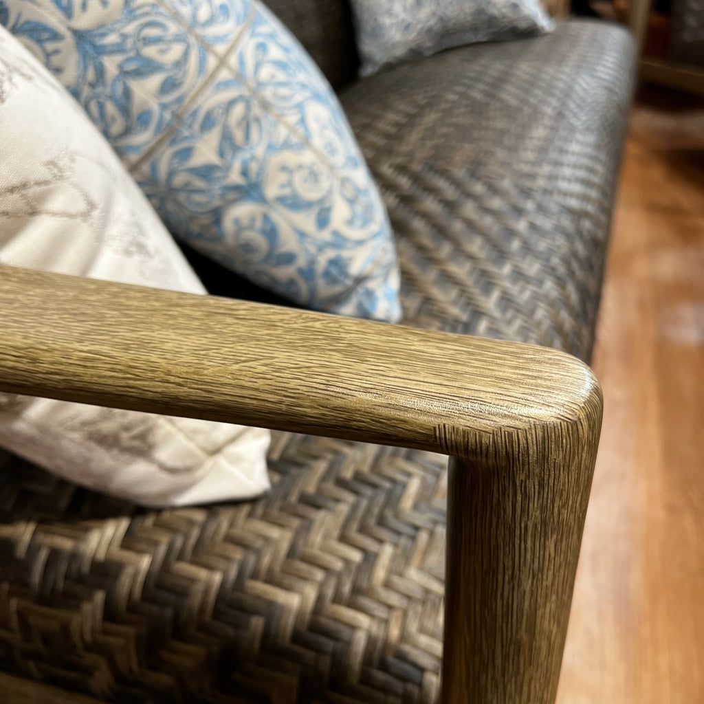 Close-up of a wooden armrest on the Provence 4 pc. Sofa from Delivery Only, featuring all-weather wicker and blue-patterned cushions, set on a wooden floor to create a cozy outdoor space.