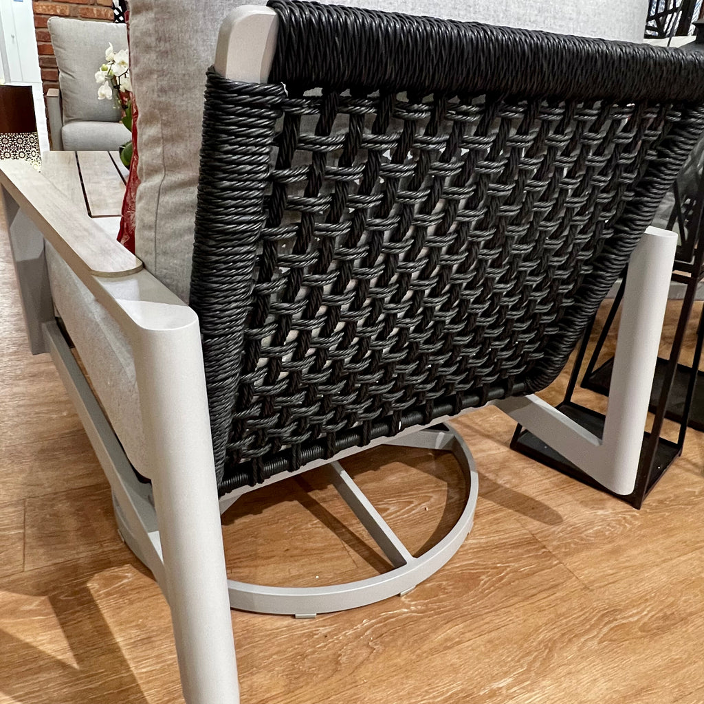 Close-up of a modern chair from the Delivery Only Titan 4-Piece Outdoor Patio Set, showcasing a metal frame with woven black rope backrest. Premium cushions on wooden flooring blend contemporary and rustic elements, ideal for outdoor spaces.