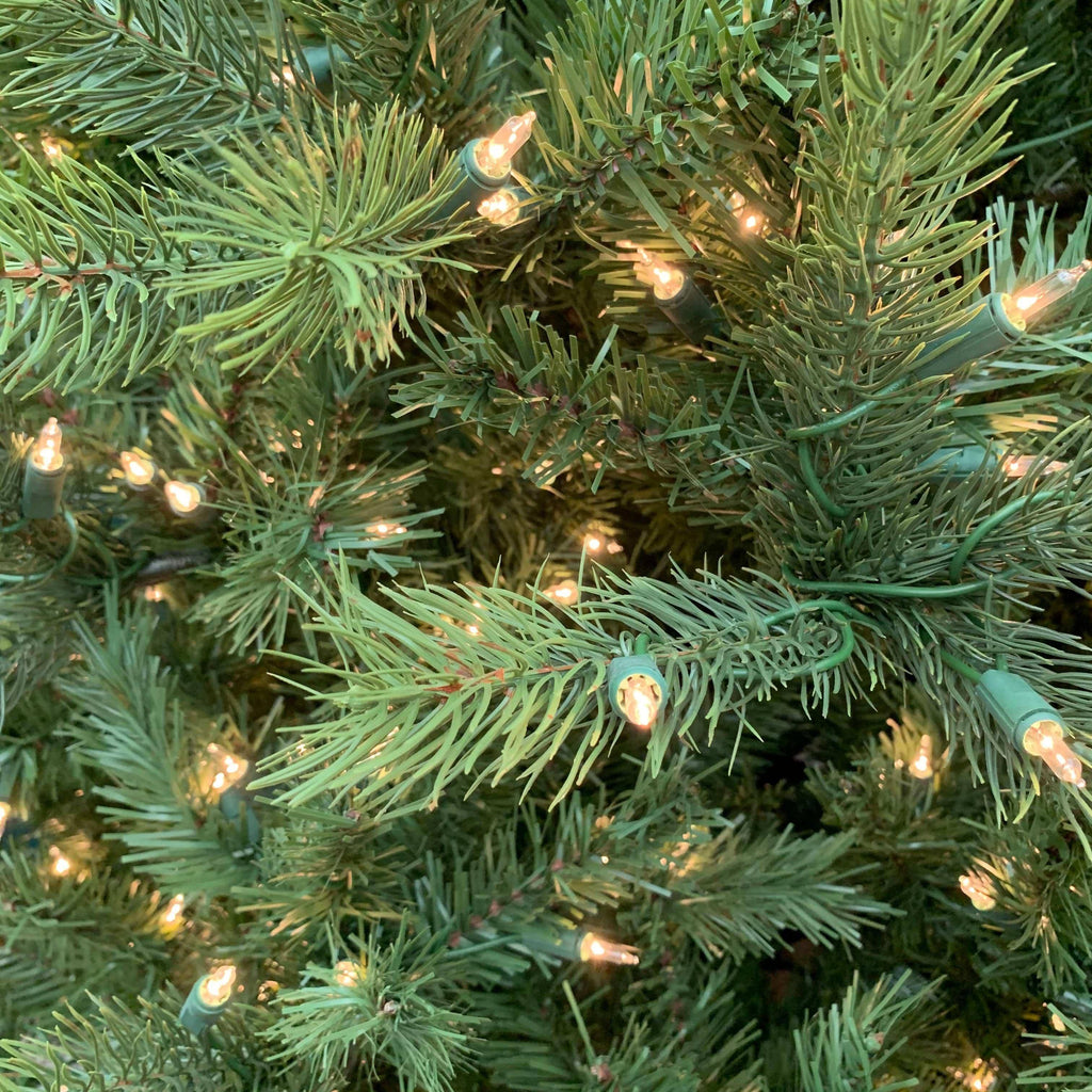 Close-up of a lifelike Kensington Fir Multi-Function Lights 6.5 Ft. artificial Christmas tree decorated with small, glowing string lights.