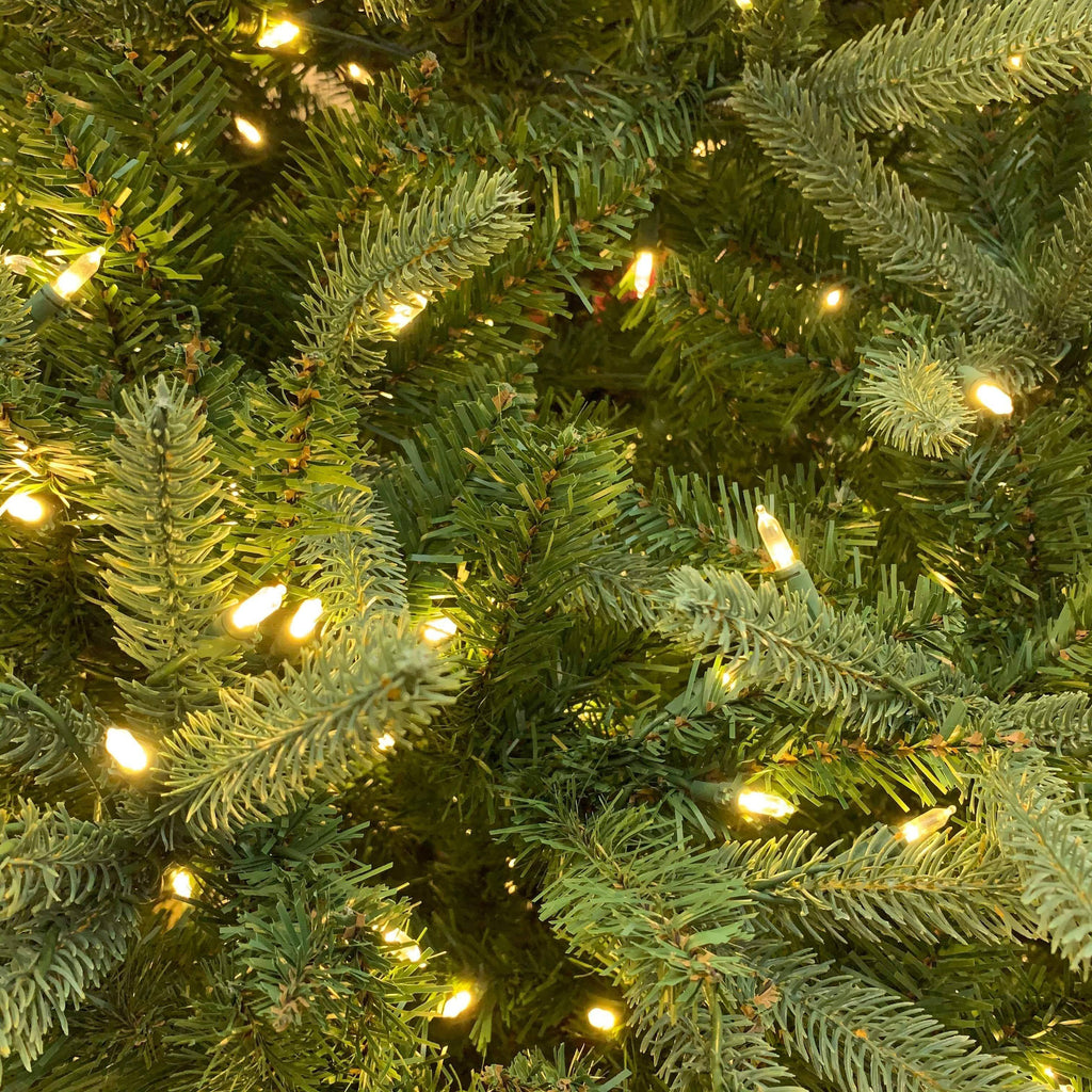A close-up of the 9 ft. Wyoming Fir by Available for Pick-up & Delivery features lifelike green needles and warm white LED lights, creating a cozy, festive atmosphere.