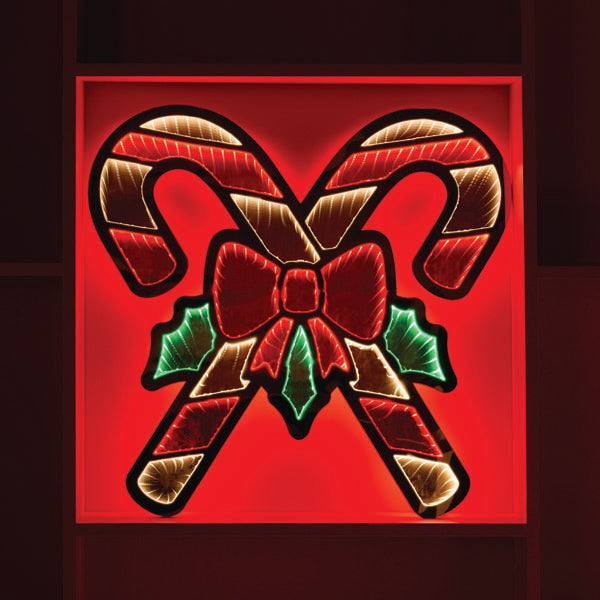The Infinity Light – Double Candy Cane by Available for Pick-Up & Delivery is a 22.5” neon sign with crossed red and white-striped candy canes, a red bow, and green holly leaves that glow brilliantly against a bright red background, creating perfect holiday decor.