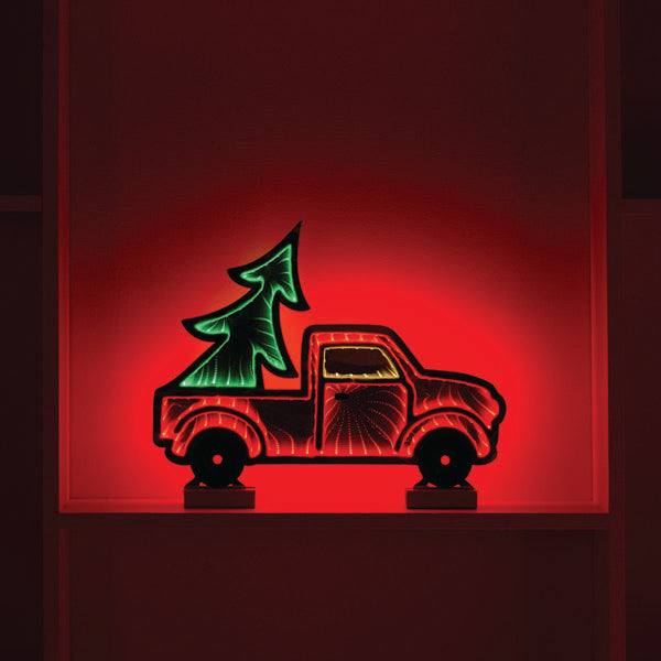 Infinity light Christmas decoration of a red pick up ruck with a large Christmas tree in the back. The backdrop is lit with red lights.