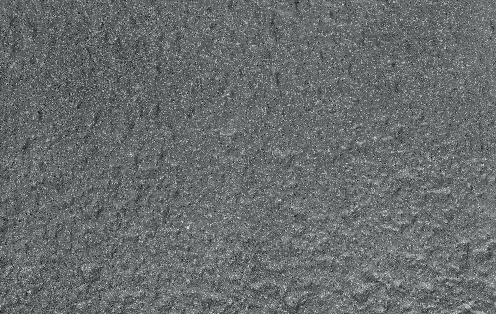 A close-up of dark gray, textured asphalt makes an ideal setting for the Blackburn Divider Planter - Grey (26x10) by Pickup & Local Delivery Only, perfect for city sidewalks needing durable, weather-resistant fiberglass planters.