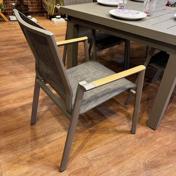 The Aspect Slat Outdoor Patio Extension Dining Set (11 pc.) from Delivery Only includes a modern dining chair with a gray mesh back and seat, beige armrests, and exudes modern elegance on a wooden floor beside a partially set matching table for an inviting dining experience.