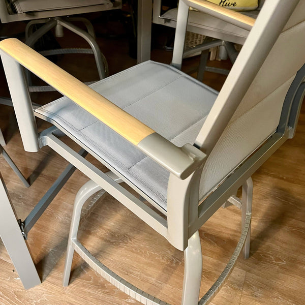 The Bozania Outdoor Bar Dining 5-Piece Set by Delivery Only includes a gray metal high chair with a padded seat, teak-accented wooden armrests, and footrest. It elegantly complements the surrounding furniture on your wooden floor.