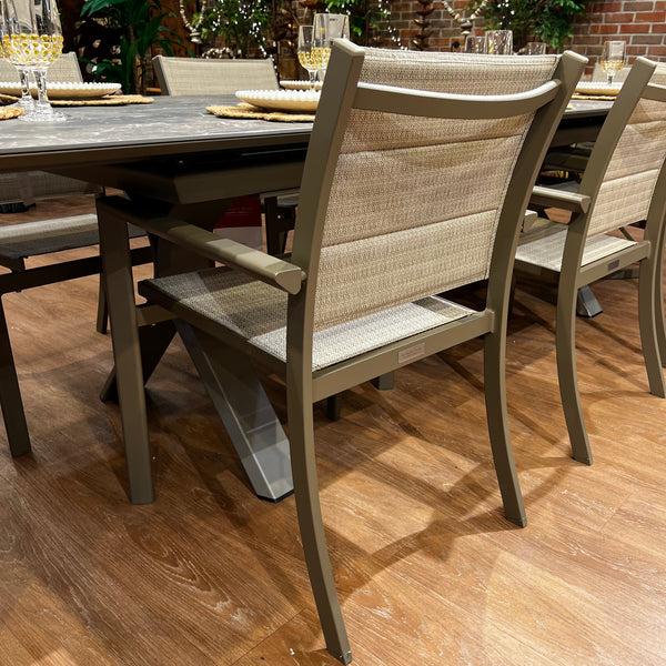 Introducing the Horizon Outdoor Patio Dining Set – 7pc. by Delivery Only: an outdoor set with a gray-topped rectangular table and cushioned brown chairs featuring textured backs and seats. Made with UV-resistant materials, its perfect for any backyard with brick walls and greenery accents.