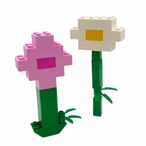 Two LEGO flowers built at the Pick-Up Only LEGO® Make-and-Take Workshop (March 7, 11AM) stand upright with green stems—one pink with a magenta center, one white with yellow—against a plain background.